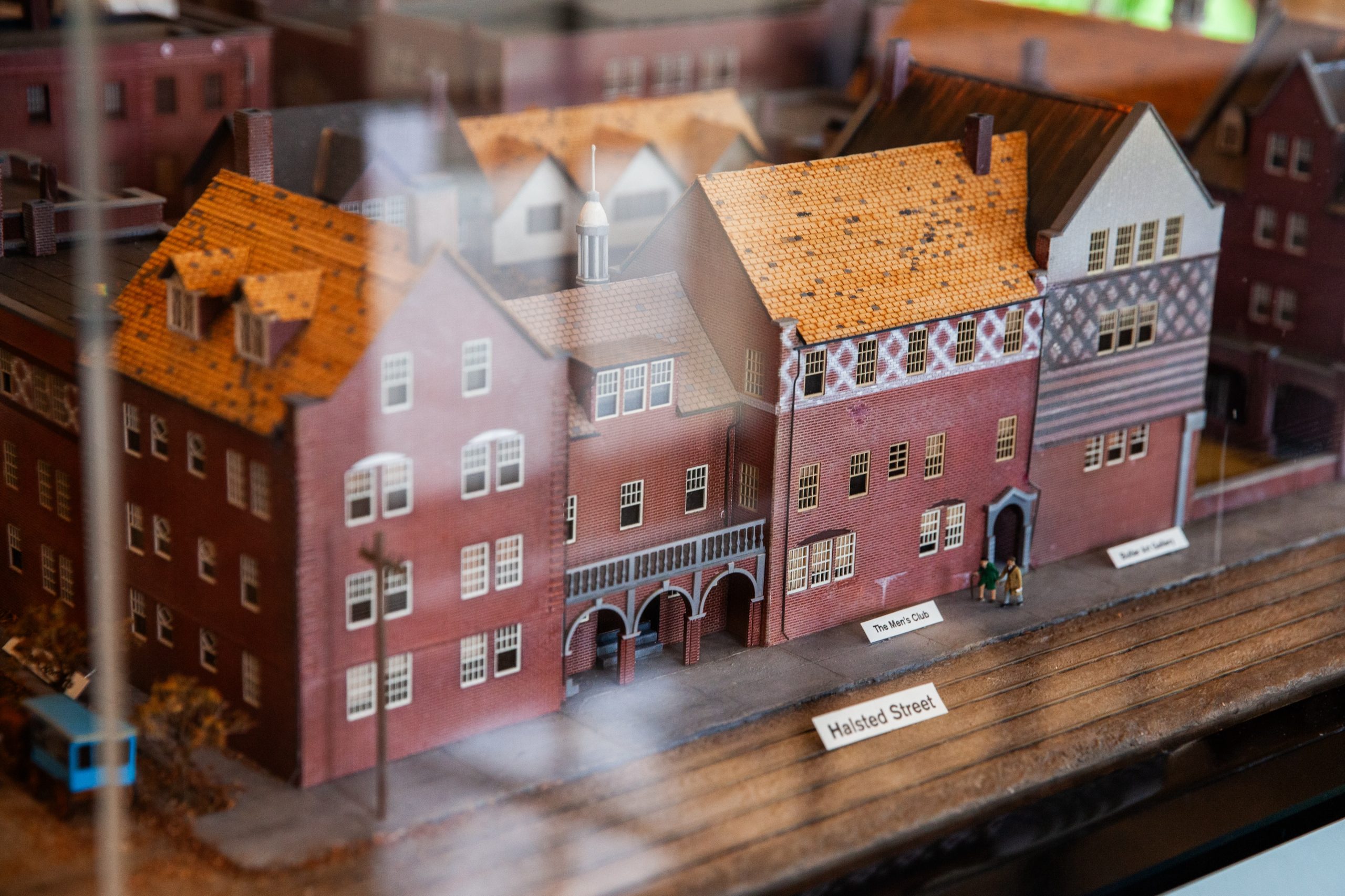 A close-up of a detailed miniature model of brick buildings, labeled “Halsted Street,” with train tracks in the foreground and small signs identifying locations.