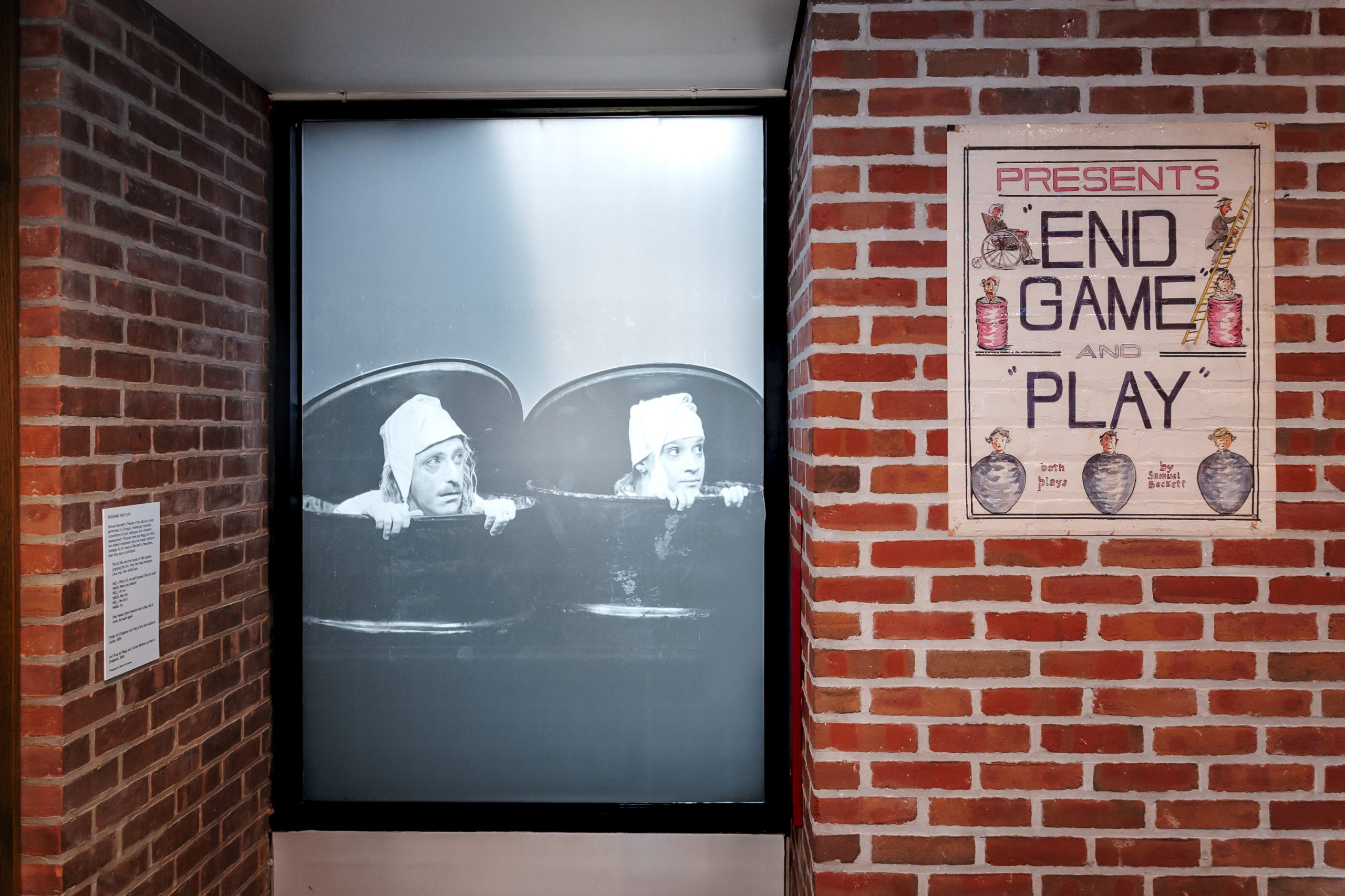 A black-and-white photo shows two people in hats peeking over a tub. Next to it, a vintage-style poster on a brick wall reads Presents End Game and Play with illustrations of trophies and faces.