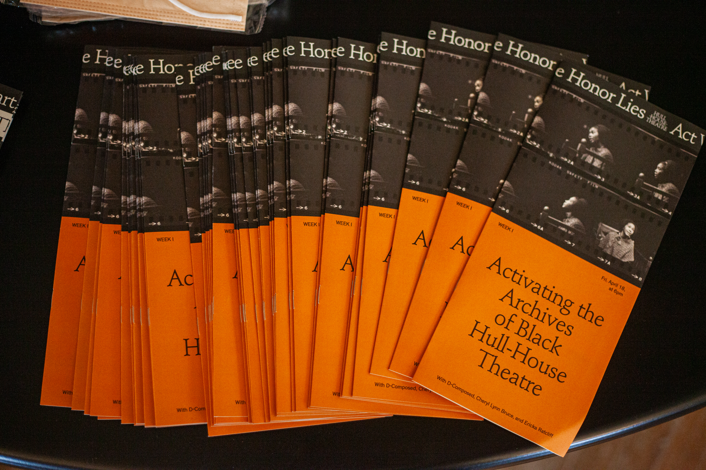 Several orange and black event programs are arranged in a fan shape on a dark surface. The covers read, Activating the Archives of Black Hull-House Theatre.