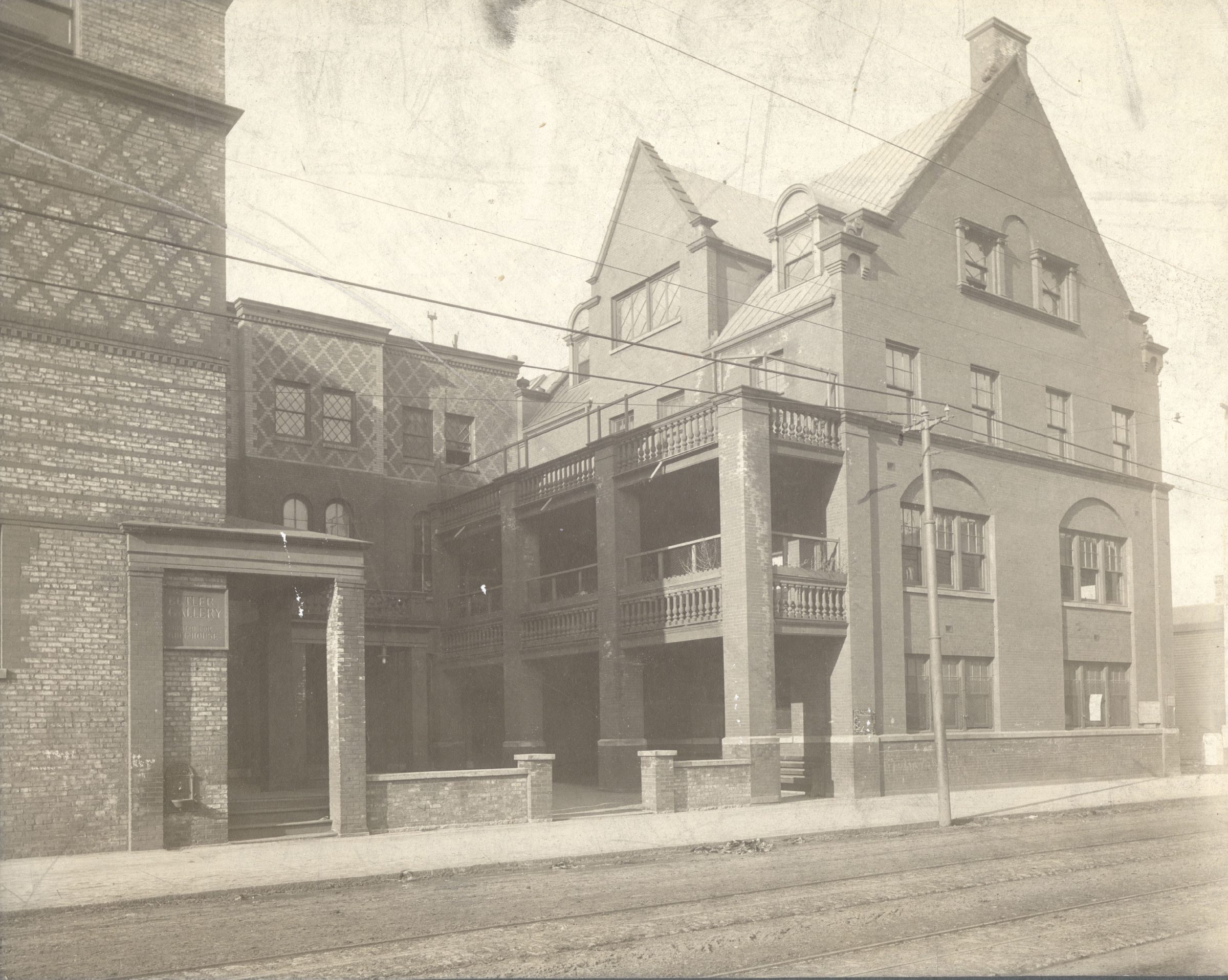 A sepia-toned photo of a large brick building with balconies, arched windows, and ornate details, adjacent to a dirt road and streetcar tracks.