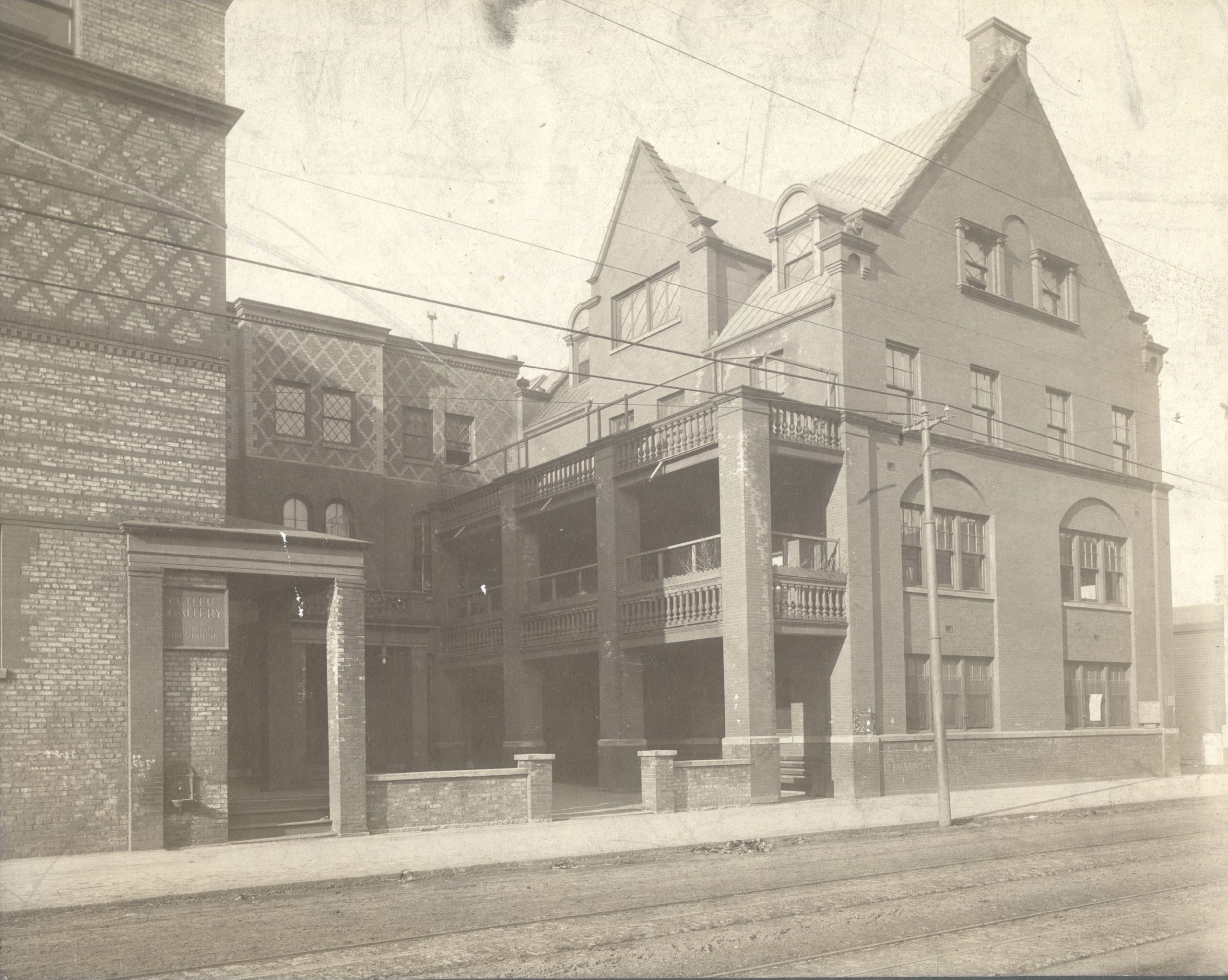A sepia-toned photo of a large brick building with balconies, arched windows, and ornate details, adjacent to a dirt road and streetcar tracks.