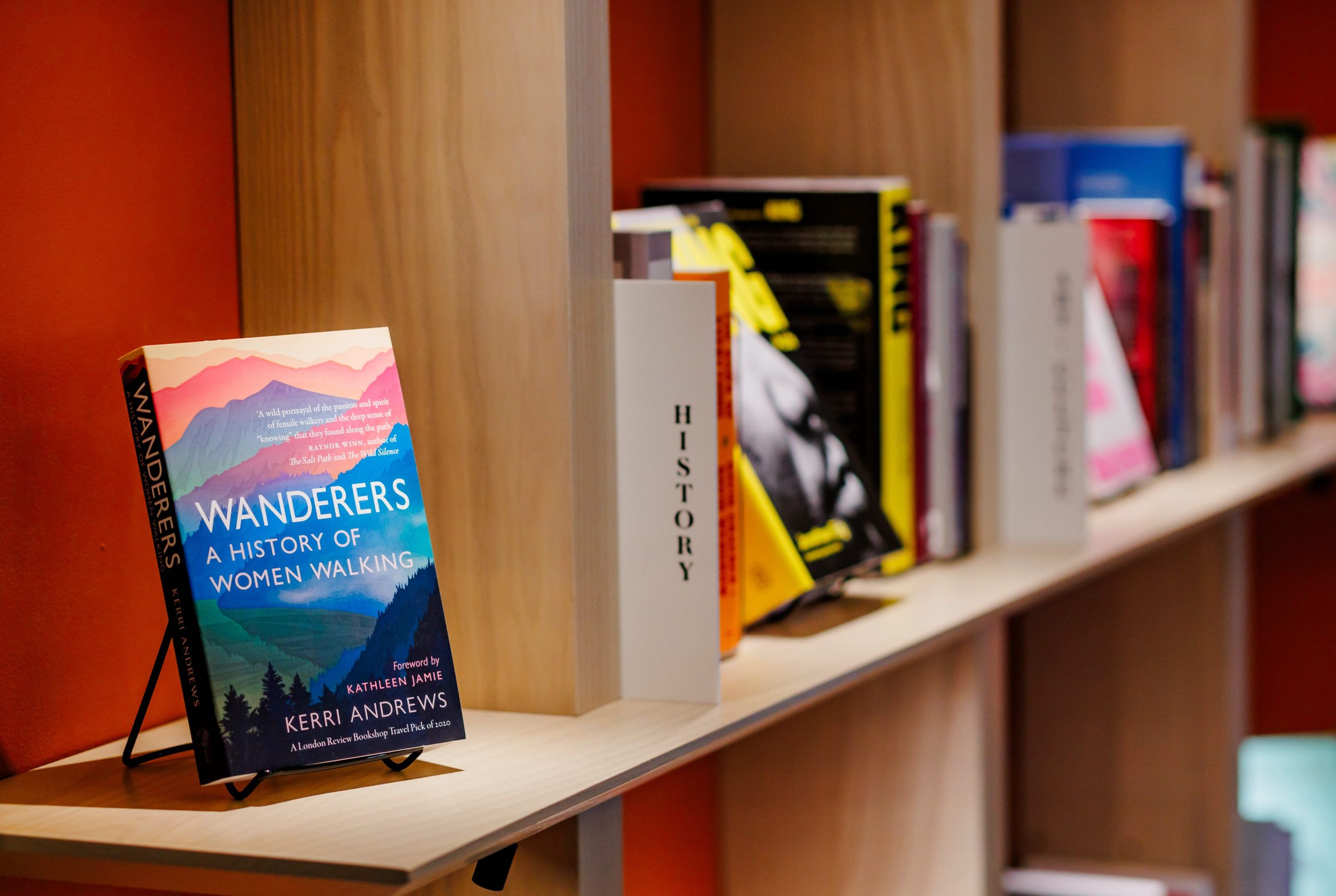 A bookshelf with various books, including Wanderers: A History of Women Walking by Kerri Andrews displayed prominently on a stand, and a section labeled History.