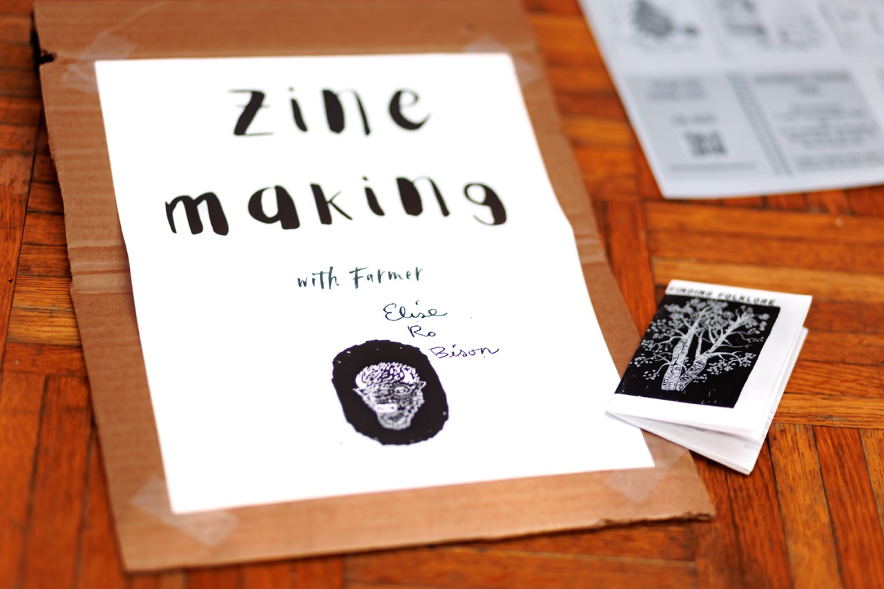A printed zine cover titled Zine Making with Farmer, featuring an illustrated skull and the names Elise, Ro, and Bison, rests on cardboard next to a small, folded black-and-white booklet.