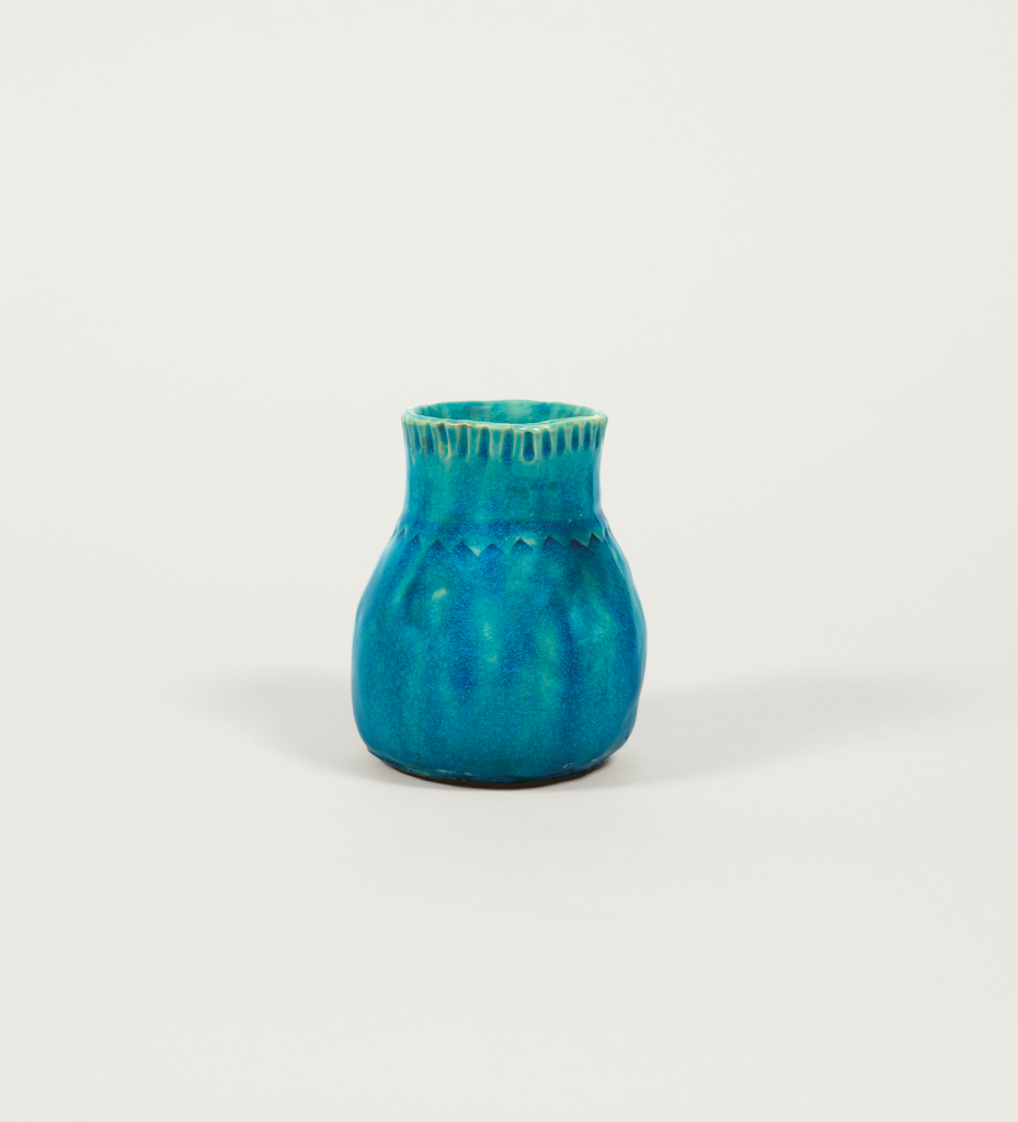 A small, round, blue ceramic vase with a narrow opening and textured detailing near the rim, set against a plain white background.