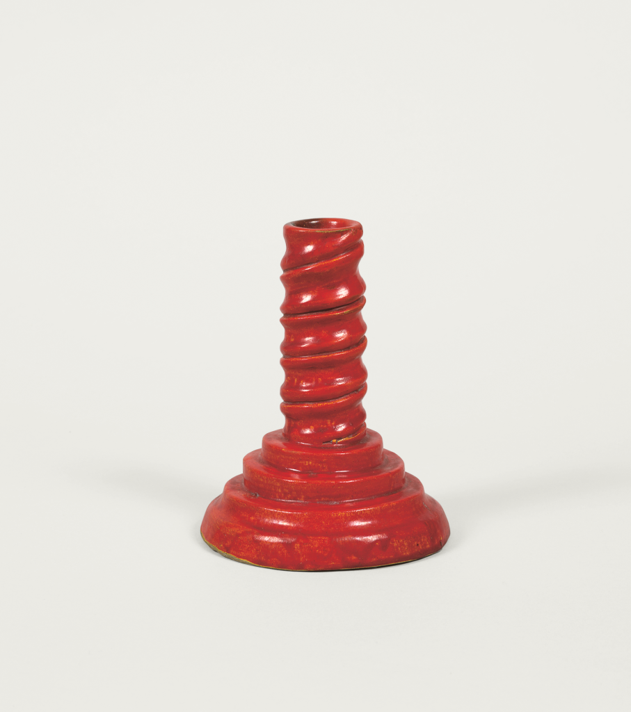 A small, red, spiral-shaped candlestick holder with a wide, tiered base and a twisted central stem, set against a plain white background.