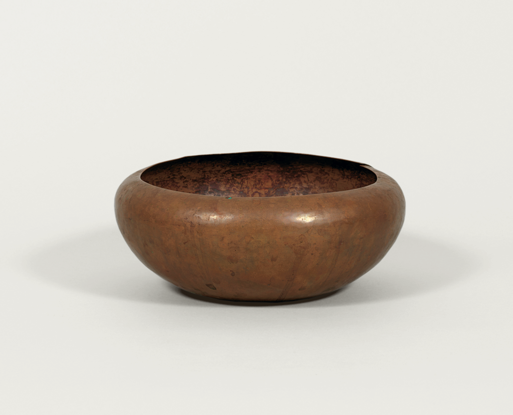 A round, shallow copper bowl with a smooth, unadorned surface and a slightly uneven rim, set against a plain white background.