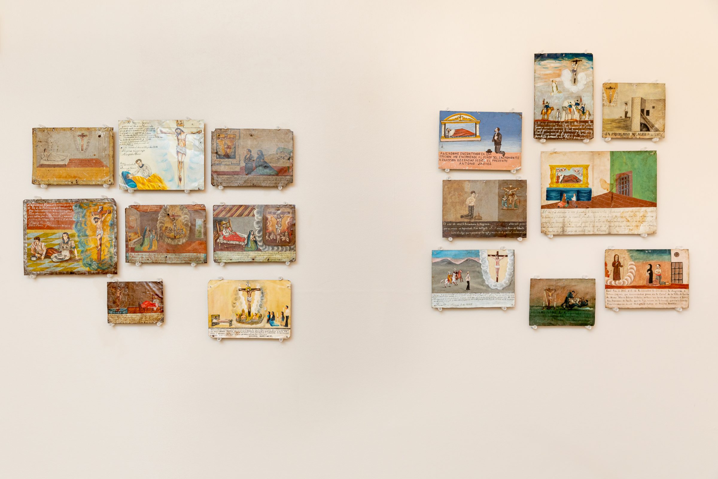 Two groups of small, colorful paintings with handwritten text, displayed on a white wall. Each painting depicts various scenes with people, objects, and landscapes in a folk art style.