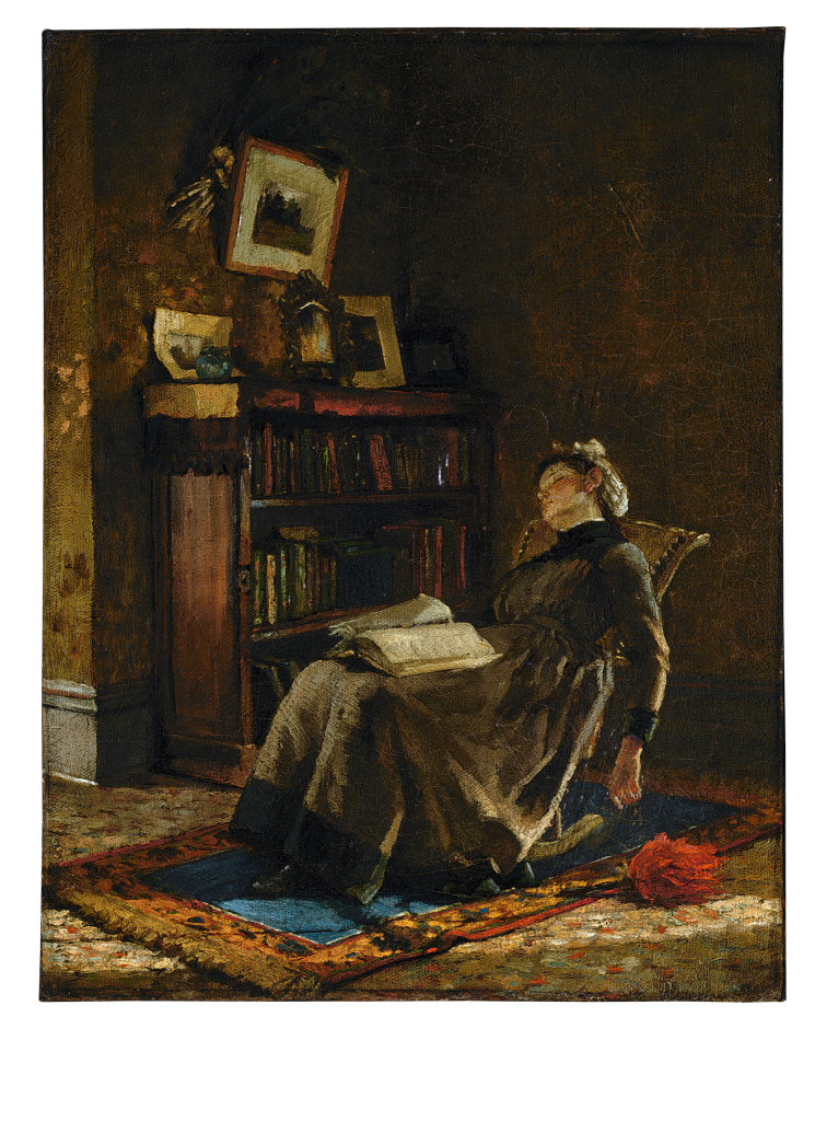 A woman in a long dark dress reclines in a chair with a book open on her lap in a dimly lit room. Behind her is a bookshelf, framed pictures, and a cabinet; a bright rug and a red object are on the floor.