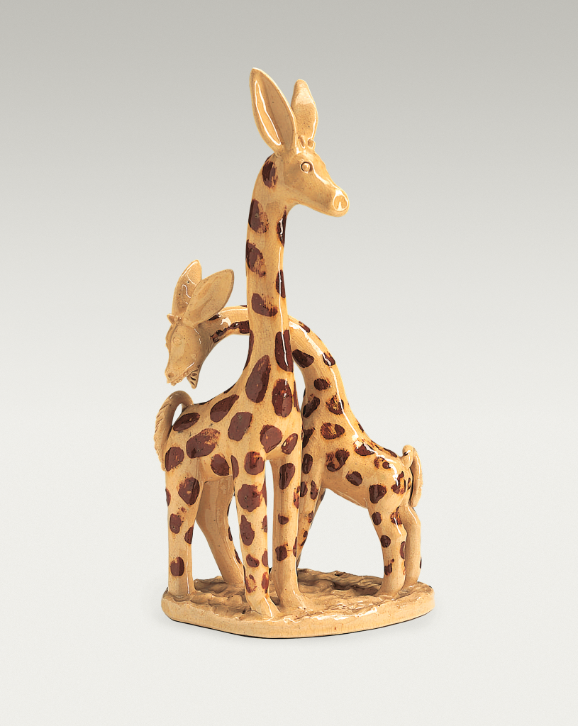A ceramic sculpture of two stylized giraffes with long necks, spotted patterns, and exaggerated features, standing closely together on a flat base against a plain background.