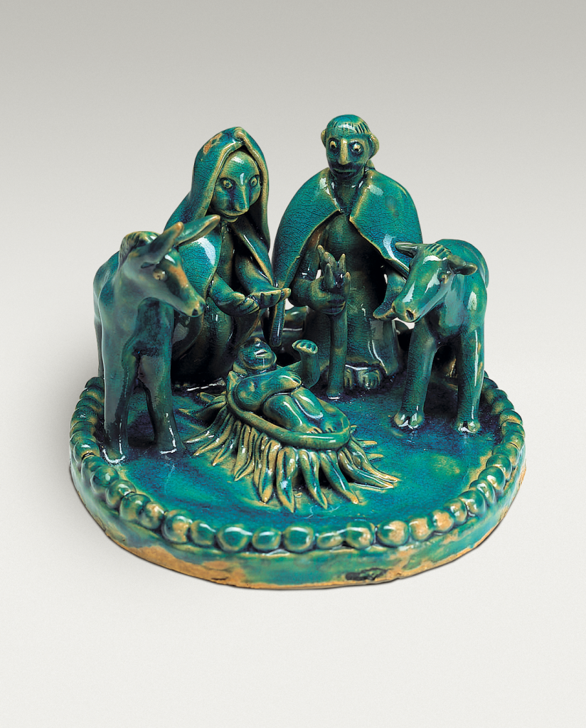 A green ceramic nativity scene features Mary, Joseph, baby Jesus in a manger, a cow, and a donkey, all arranged on a round base with a braided edge.