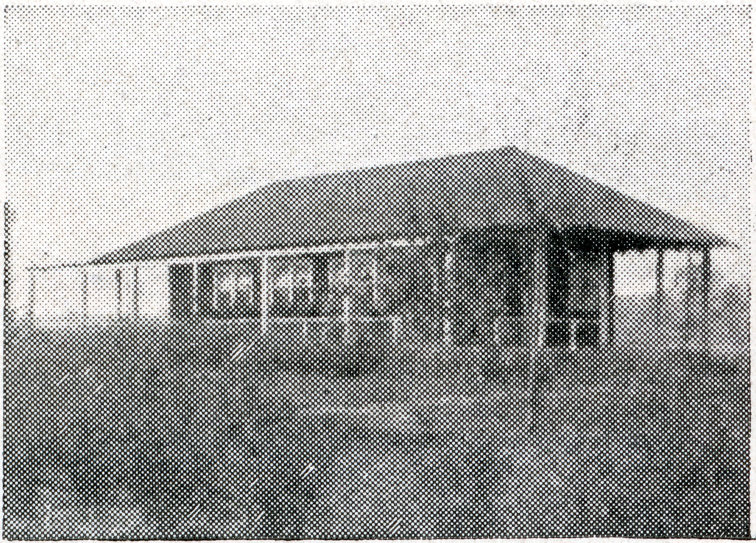 A black and white, pixelated photo of a simple, single-story building with a large roof and open sides, surrounded by grass.