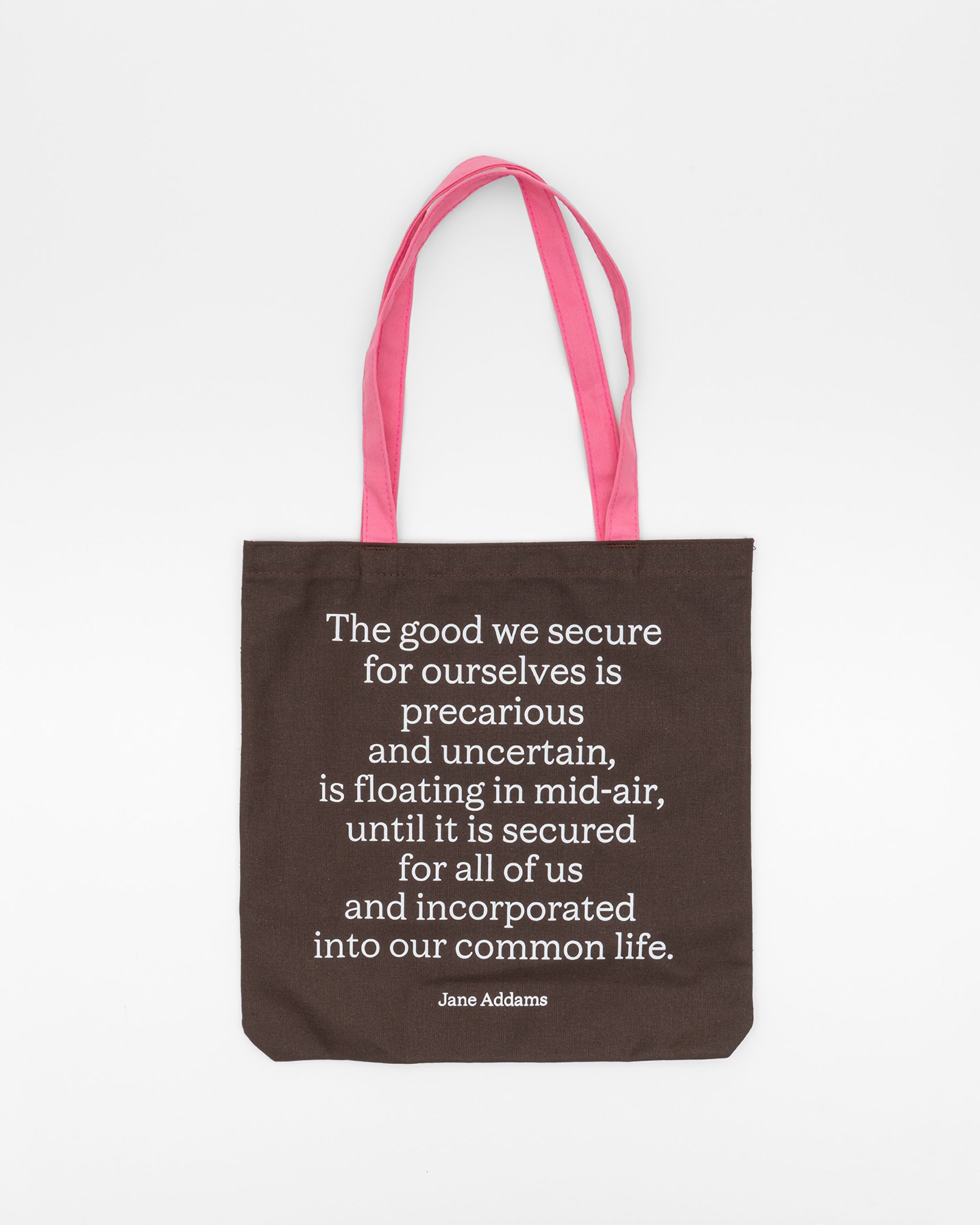 A brown tote bag with pink handles displays a Jane Addams quote in white text about the importance of securing good for everyone, not just ourselves.