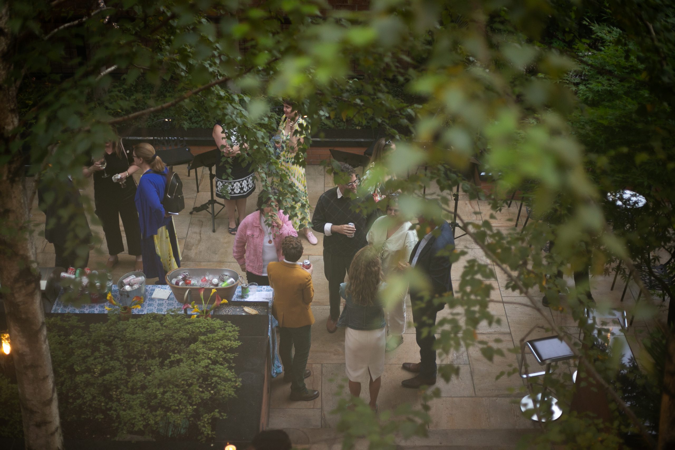 A group of people socializing and holding drinks on a stone patio during an outdoor evening gathering.