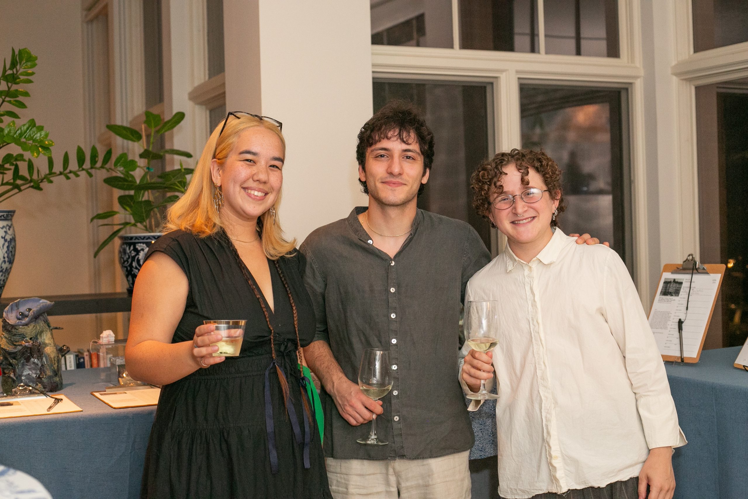 Three people standing together and holding glasses of white wine at an indoor event.