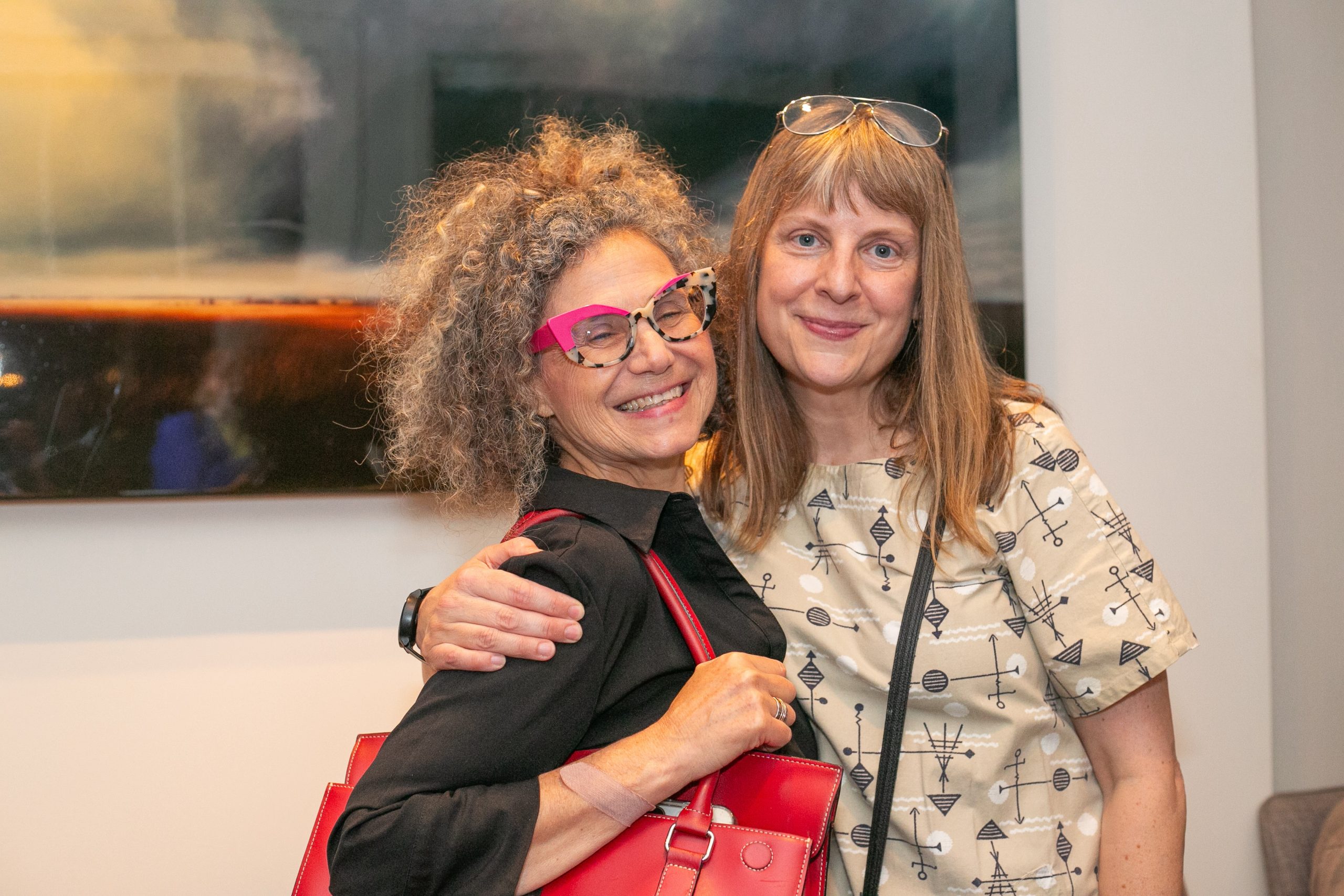 Two women smiling and posing for a photo together in an art gallery.