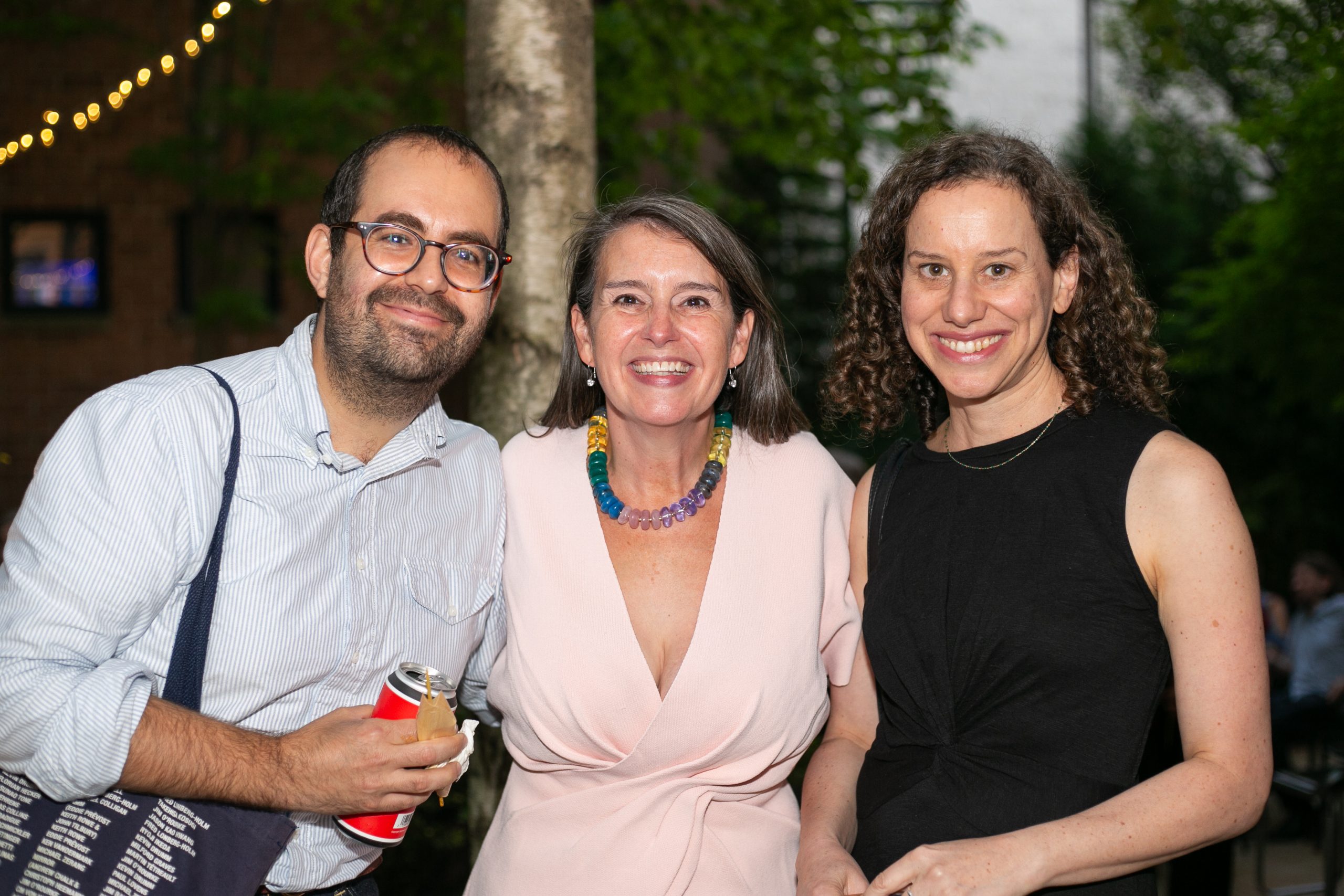 Three people smiling together outdoors at an evening event.