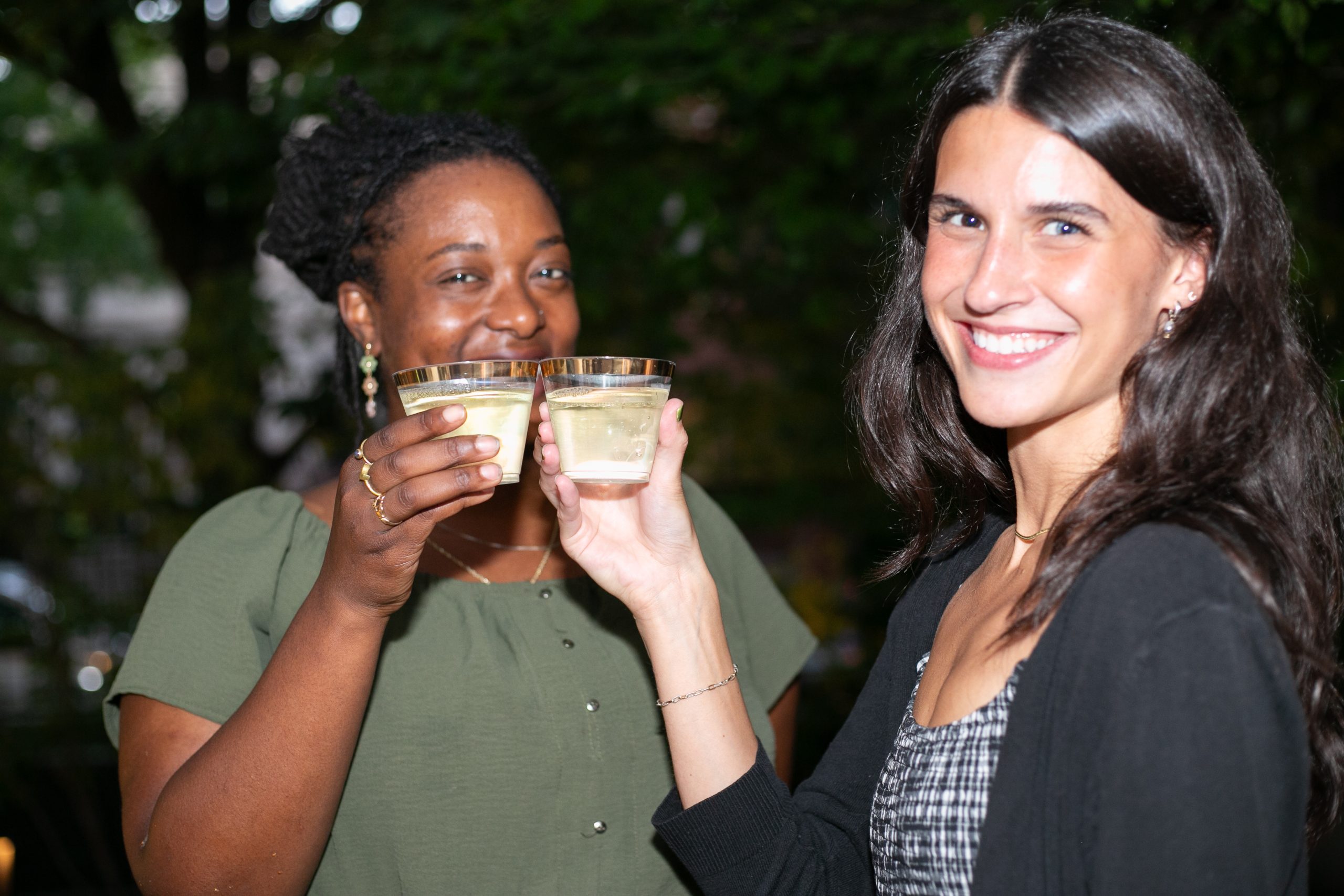 Two smiling women toast each other with glasses of white wine or champagne.