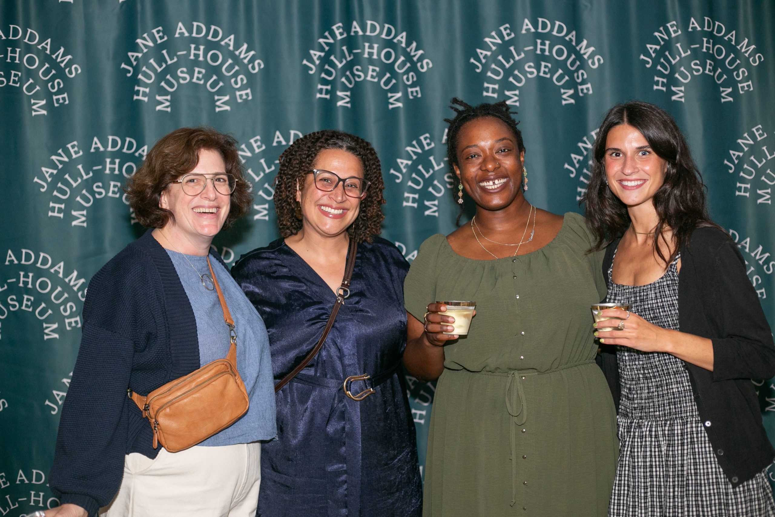 Four women smiling together in front of a Jane Addams Hull-House Museum step-and-repeat backdrop.